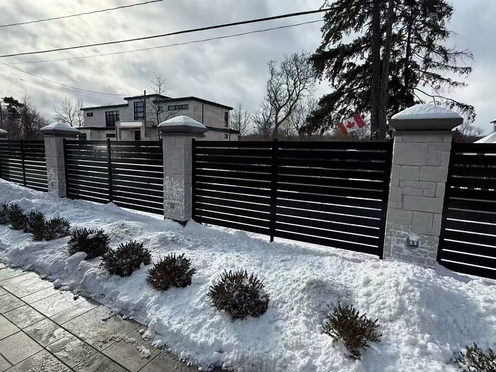 Black aluminum horizontal-slat fence standing through an Ontario winter